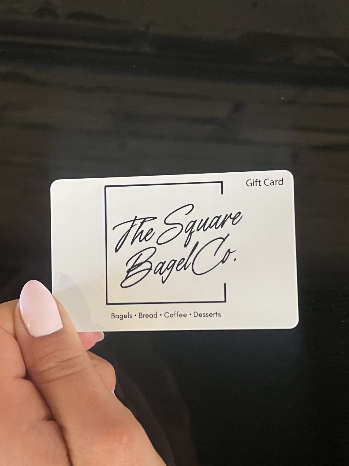 A Square Bagel Co. gift card held in front of the shop