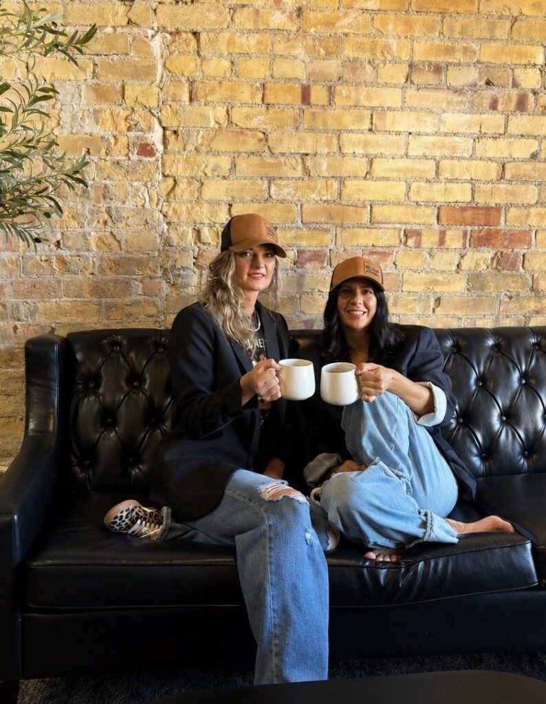 Syd and Alana, sisters-in-law and owners of The Square Bagel Co., sharing coffee on the shop’s leather couch